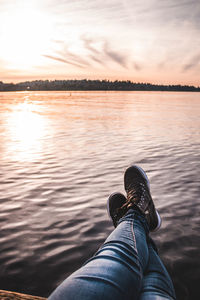 Low section of man in lake against sky during sunset