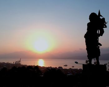 Silhouette city by sea against sky during sunset