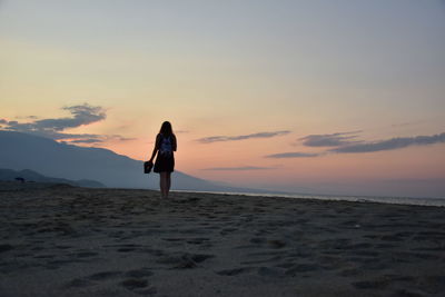 Rear view of woman standing on beach during sunset