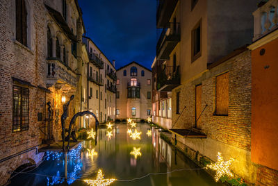 Illuminated buildings by canal at night