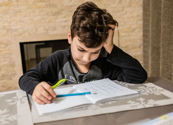 Cheerful and funny schoolboy solves  homework emotionally. thinks about how to solve math examples 