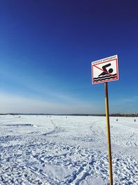 Road sign on snow covered land against clear blue sky