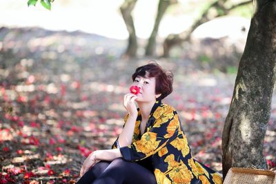 Portrait of woman smelling flower while sitting by tree