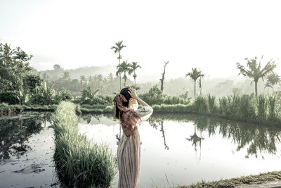 Woman standing by lake against sky