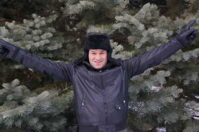 Smiling man standing with arms raised against tree