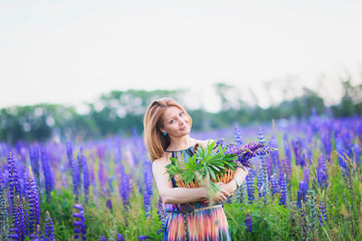 Young attractive woman holding a basket full of lupine flowers