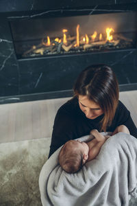 Mother with daughter sitting against fireplace at home