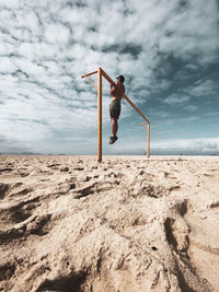 Low angle view of man exercising at beach against sky