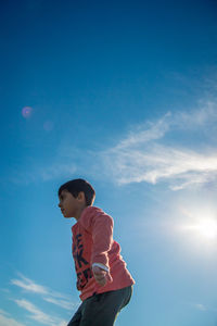 Low angle view of boy standing against blue sky