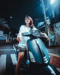 Portrait of a smiling young woman sitting in city at night