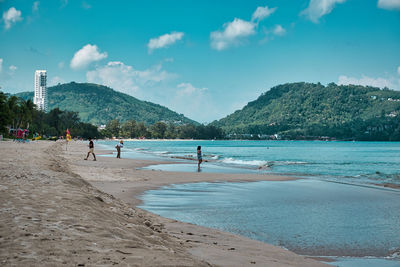 People on beach by mountain against sky