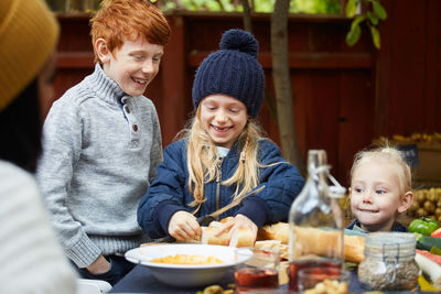 Girl cutting bread while standing by siblings at table for garden party