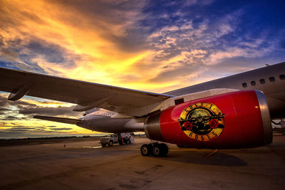 Airplane on airport runway against sky at sunset