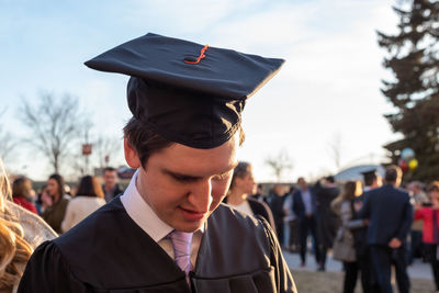 Close-up of young man wearing graduation gown against sky