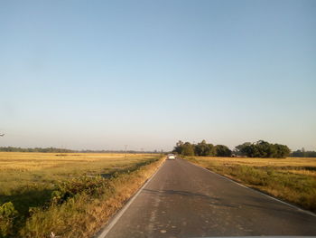 Road amidst field against clear blue sky