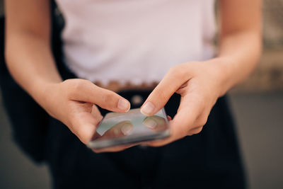 Midsection of young woman text messaging through mobile phone in city