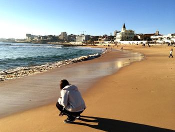 Rear view of woman standing on beach against clear sky