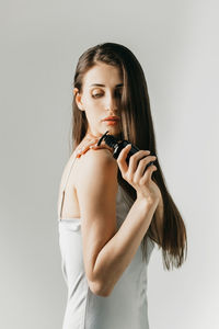 A beautiful brunette girl with long hair holds a brown dispenser with an organic cosmetic product. 