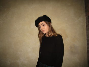 Young woman looking away while standing against wall