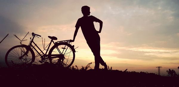 Silhouette man standing by bicycle against sky during sunset