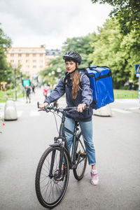 Portrait of confident food delivery woman with bicycle on street in city