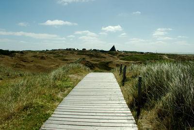 Boardwalk leading towards landscape against sky