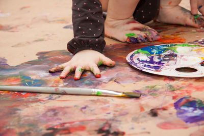 Little girl playing with paint on the floor with bare hands 