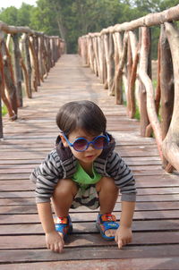 Boy wearing sunglasses while crouching on footbridge