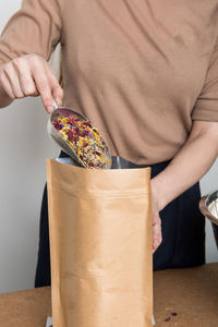 Midsection of woman filling petals in paper bag at home