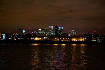 Illuminated cityscape by sea against sky at night