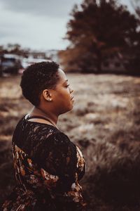 Side view of woman looking away while standing at field