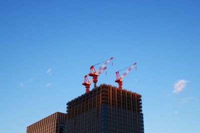 Low angle view of crane by building against sky