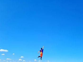 Low angle view of men paragliding against clear blue sky