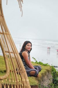 Portrait of smiling young woman sitting on shore by sea against sky