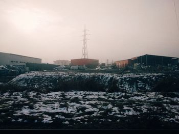 Snow covered land and buildings against sky during sunset