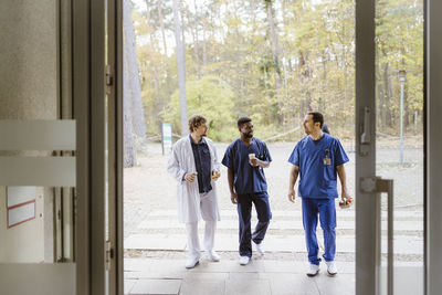 Full length of male healthcare workers talking while walking towards hospital entrance