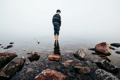 Man standing on rock by sea against sky