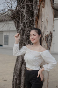 Portrait of smiling young woman standing on tree trunk