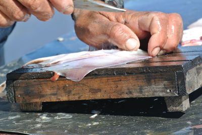 Cropped image of person cleaning fish on table at market