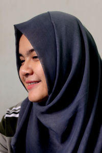 Close-up of young woman wearing hijab looking away against wall at home