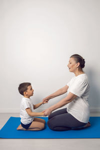 Grandmother and her grandson are sitting on a yoga mat in a white apartment at home