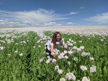 Young woman with flowers on field against sky