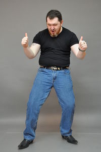 Full length of man showing thumbs up sign against gray background