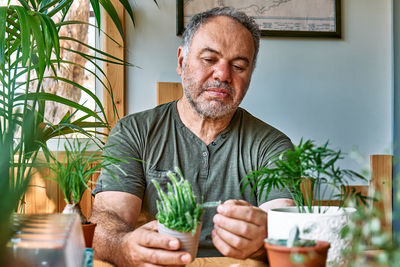 Mature bearded man holding a pot with cactus. taking care of home flowers and succulents
