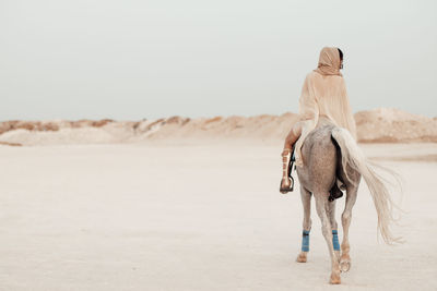 Rear view of arab woman riding horse on beach