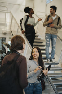 Multiracial female students discussing by staircase in university