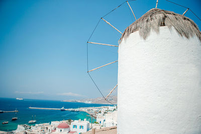 Traditional windmill by sea against clear blue sky