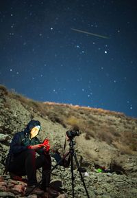 Rear view of woman sitting on mountain against sky at night