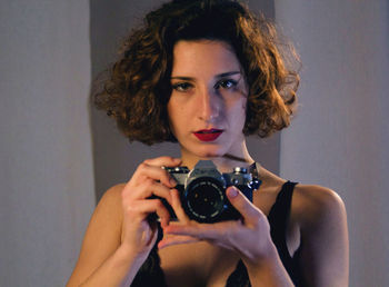 Portrait of woman holding camera against wall