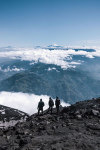 Rear view of male friends standing on cliff against sky